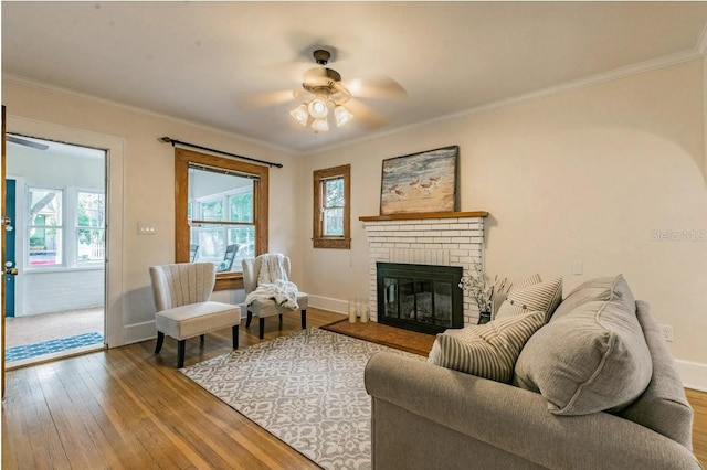 living room featuring crown molding, ceiling fan, baseboards, hardwood / wood-style floors, and a fireplace