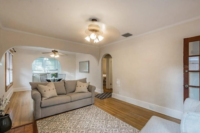 living room with arched walkways, light wood-style flooring, and crown molding