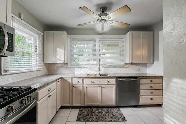 kitchen with tasteful backsplash, light stone countertops, light tile patterned floors, stainless steel appliances, and a sink