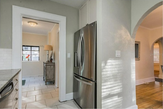 kitchen with ornamental molding, light stone counters, arched walkways, appliances with stainless steel finishes, and white cabinets