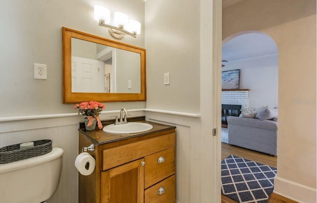 half bath with toilet, wood finished floors, a fireplace, wainscoting, and vanity