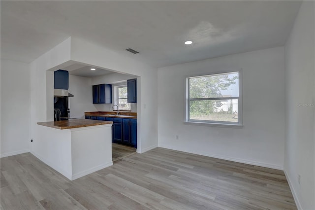 kitchen featuring light wood-type flooring, blue cabinetry, baseboards, wooden counters, and extractor fan