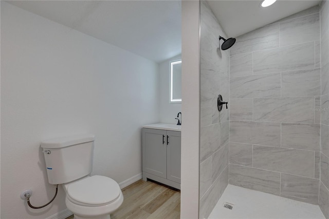 bathroom with baseboards, toilet, a tile shower, wood finished floors, and vanity