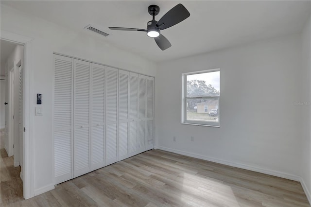 unfurnished bedroom featuring wood finished floors, visible vents, baseboards, ceiling fan, and a closet