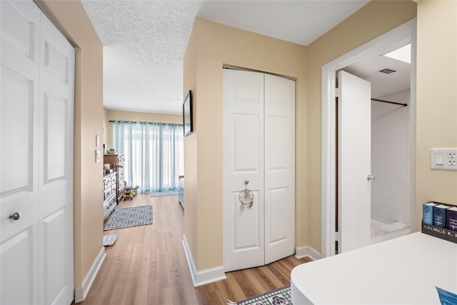 bedroom featuring light wood-type flooring, visible vents, a textured ceiling, a closet, and baseboards