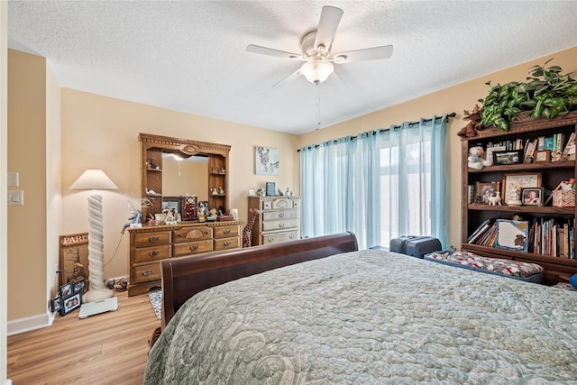 bedroom featuring baseboards, a textured ceiling, light wood-style floors, and a ceiling fan