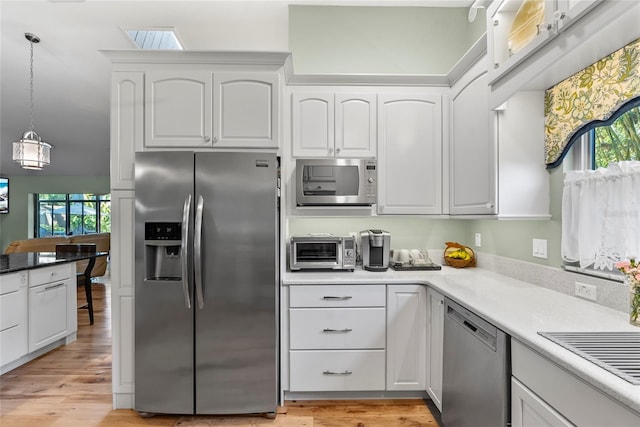 kitchen featuring light wood-style flooring, stainless steel appliances, hanging light fixtures, plenty of natural light, and white cabinetry