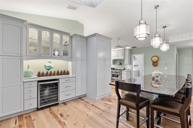 dining space with visible vents, vaulted ceiling, wine cooler, light wood-style floors, and a dry bar