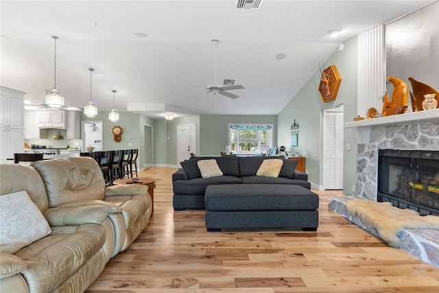 living area with visible vents, ceiling fan, light wood-type flooring, a fireplace, and high vaulted ceiling