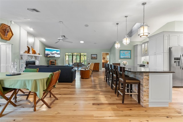 kitchen featuring a breakfast bar area, light wood finished floors, stainless steel refrigerator with ice dispenser, a tiled fireplace, and open floor plan