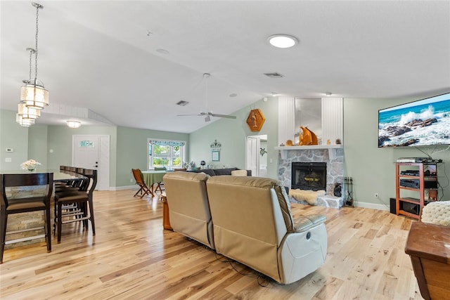 living area with visible vents, baseboards, lofted ceiling, a fireplace, and light wood-style floors