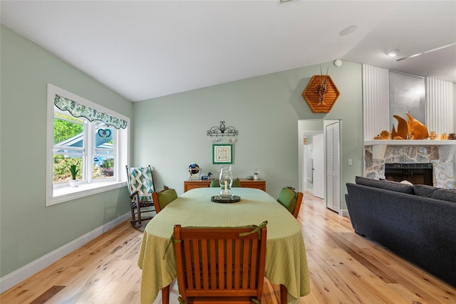 dining area with a stone fireplace, baseboards, light wood-style floors, and vaulted ceiling