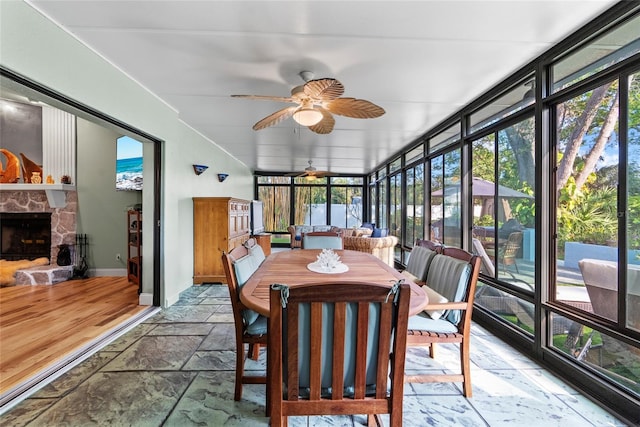 sunroom / solarium featuring a stone fireplace and ceiling fan