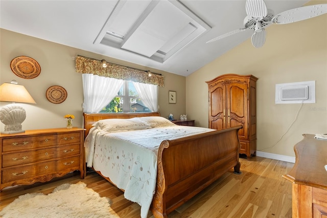 bedroom featuring a wall unit AC, baseboards, vaulted ceiling, and light wood finished floors