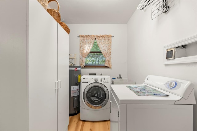 clothes washing area featuring a sink, light wood-style floors, washing machine and dryer, and water heater