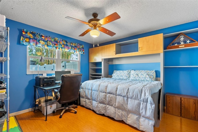 bedroom featuring a ceiling fan, wood finished floors, baseboards, and a textured ceiling