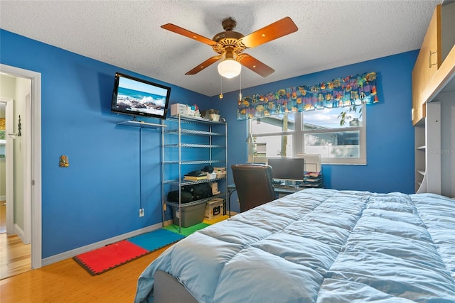 bedroom featuring a ceiling fan, wood finished floors, baseboards, and a textured ceiling