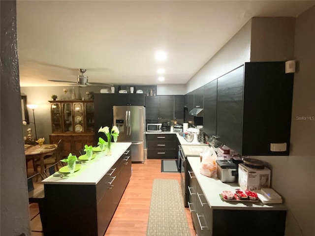 kitchen with stainless steel appliances, light wood finished floors, a kitchen island, and light countertops