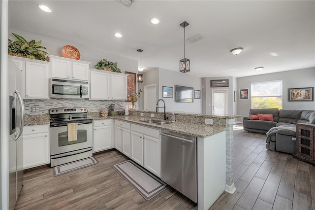 kitchen featuring appliances with stainless steel finishes, a peninsula, wood finished floors, white cabinetry, and a sink