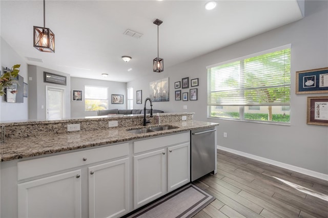 kitchen featuring wood finished floors, a sink, hanging light fixtures, white cabinets, and stainless steel dishwasher