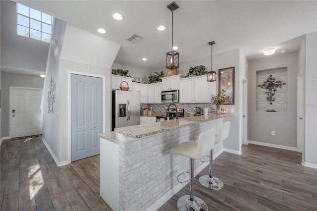 kitchen with light stone countertops, a peninsula, appliances with stainless steel finishes, white cabinetry, and backsplash