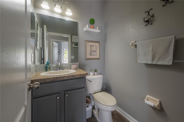 half bathroom with vanity, toilet, wood finished floors, and baseboards