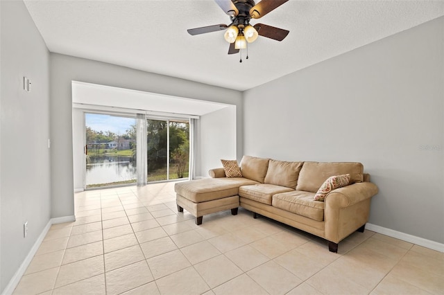 living area featuring light tile patterned flooring, a textured ceiling, a ceiling fan, and baseboards