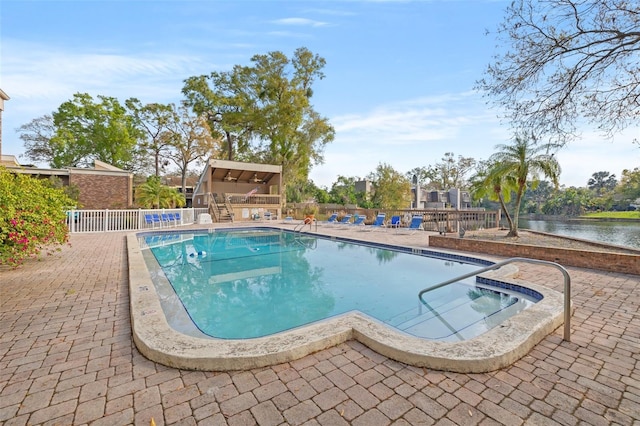 community pool with a water view, a patio, and fence