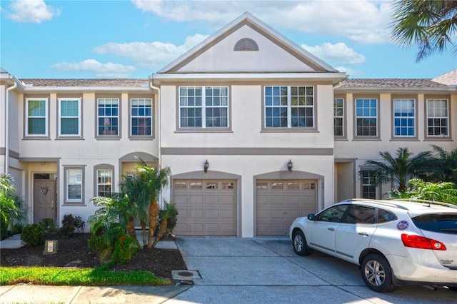 townhome / multi-family property with a garage, driveway, and stucco siding