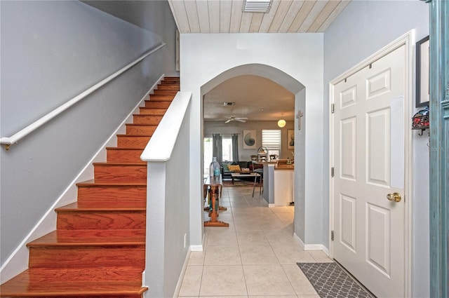 foyer with light tile patterned floors, a ceiling fan, baseboards, arched walkways, and stairs