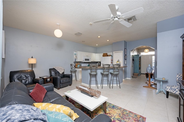 living room with a ceiling fan, a textured ceiling, arched walkways, light tile patterned floors, and baseboards