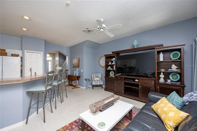 living room featuring a ceiling fan, a textured ceiling, arched walkways, light tile patterned floors, and baseboards