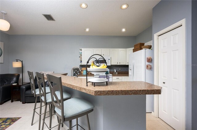 kitchen with a kitchen bar, visible vents, white cabinetry, white fridge with ice dispenser, and light tile patterned floors