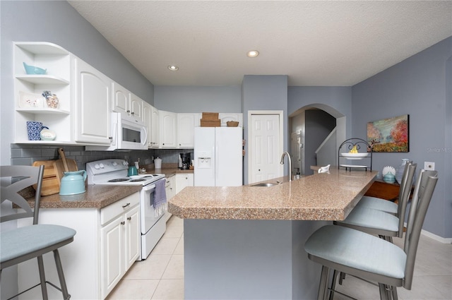 kitchen featuring white appliances, open shelves, a kitchen breakfast bar, and a sink