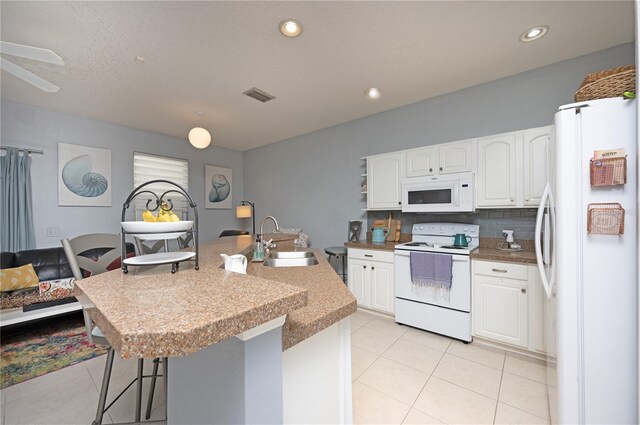 kitchen featuring white appliances, a breakfast bar area, visible vents, a sink, and white cabinets