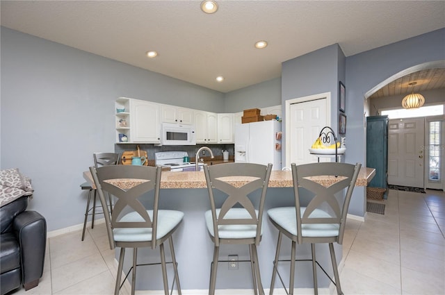 kitchen with light tile patterned flooring, white appliances, a breakfast bar, and arched walkways