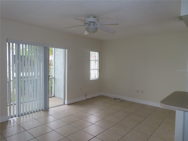 empty room featuring light tile patterned floors, a textured ceiling, baseboards, and a ceiling fan