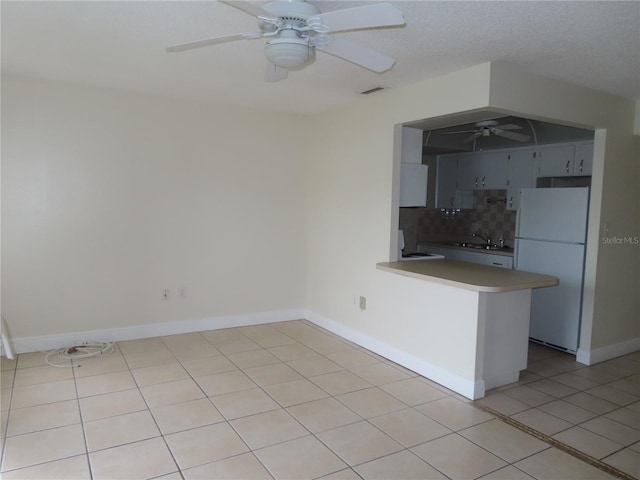 interior space featuring freestanding refrigerator, a peninsula, light tile patterned floors, decorative backsplash, and ceiling fan