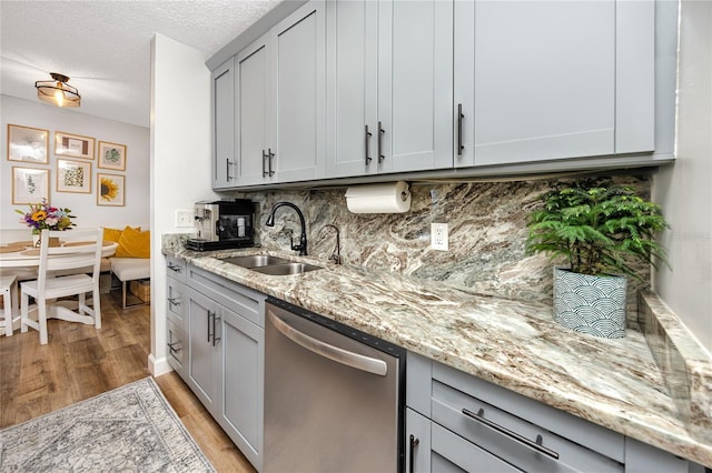 kitchen featuring light stone counters, light wood finished floors, a sink, dishwasher, and backsplash