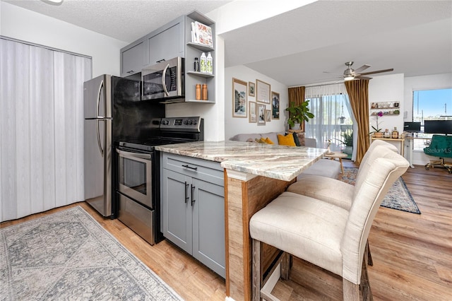 kitchen featuring stainless steel appliances, light stone countertops, open floor plan, and gray cabinets