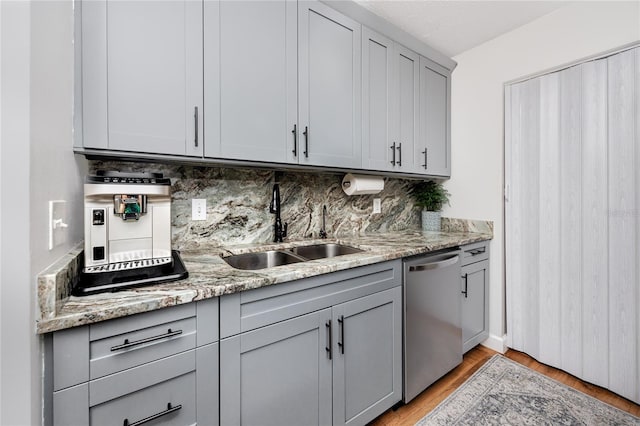 kitchen with gray cabinetry, a sink, backsplash, light wood finished floors, and dishwasher