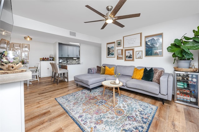 living room with wine cooler, visible vents, light wood finished floors, and ceiling fan