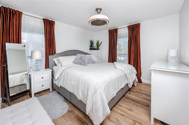 bedroom featuring baseboards, a textured ceiling, and light wood-style flooring