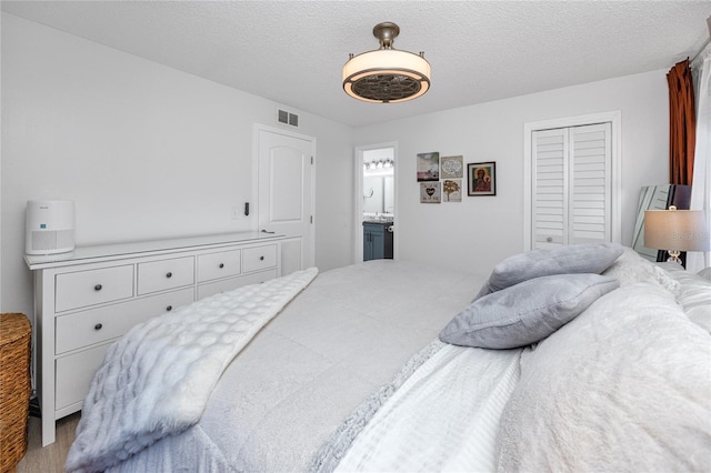 bedroom featuring visible vents, ensuite bathroom, a textured ceiling, a closet, and ceiling fan