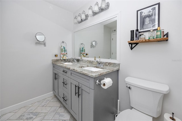 bathroom featuring double vanity, toilet, baseboards, and a sink