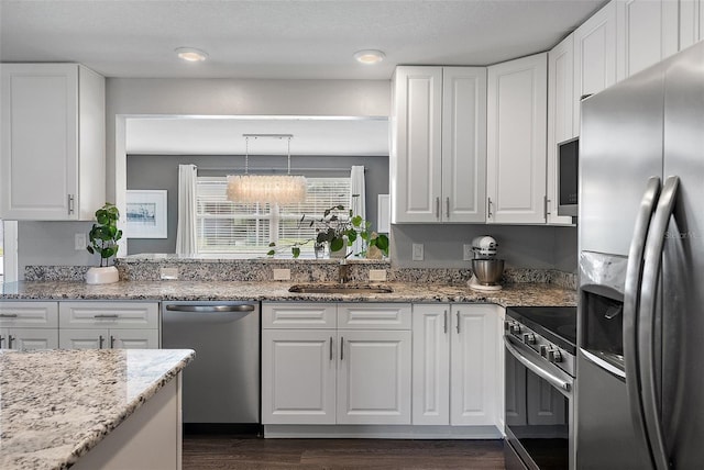 kitchen featuring light stone counters, dark wood finished floors, a sink, appliances with stainless steel finishes, and white cabinetry