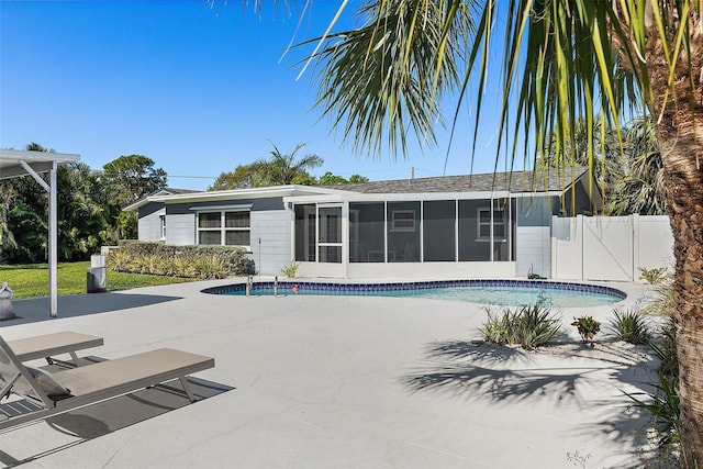 outdoor pool with a gate, a patio area, fence, and a sunroom