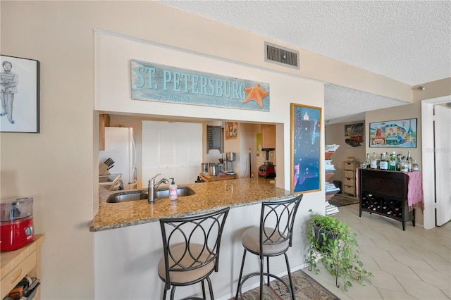 kitchen with visible vents, light stone countertops, freestanding refrigerator, a textured ceiling, and a sink