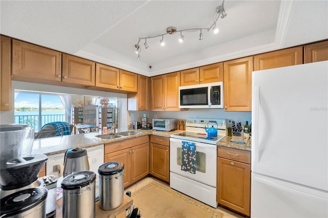 kitchen with white appliances, light stone countertops, a tray ceiling, a sink, and brown cabinets