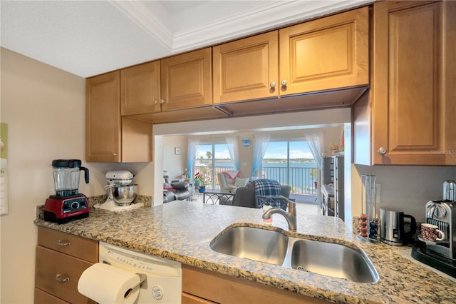 kitchen with light stone counters, brown cabinets, dishwasher, and a sink